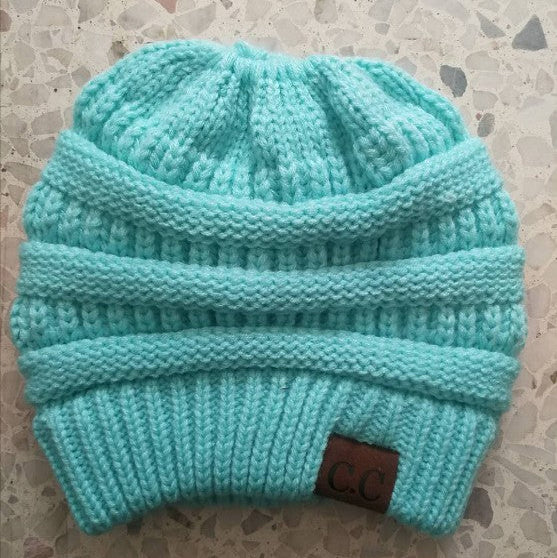 Turquoise knit beanie with a brown label on a textured surface
