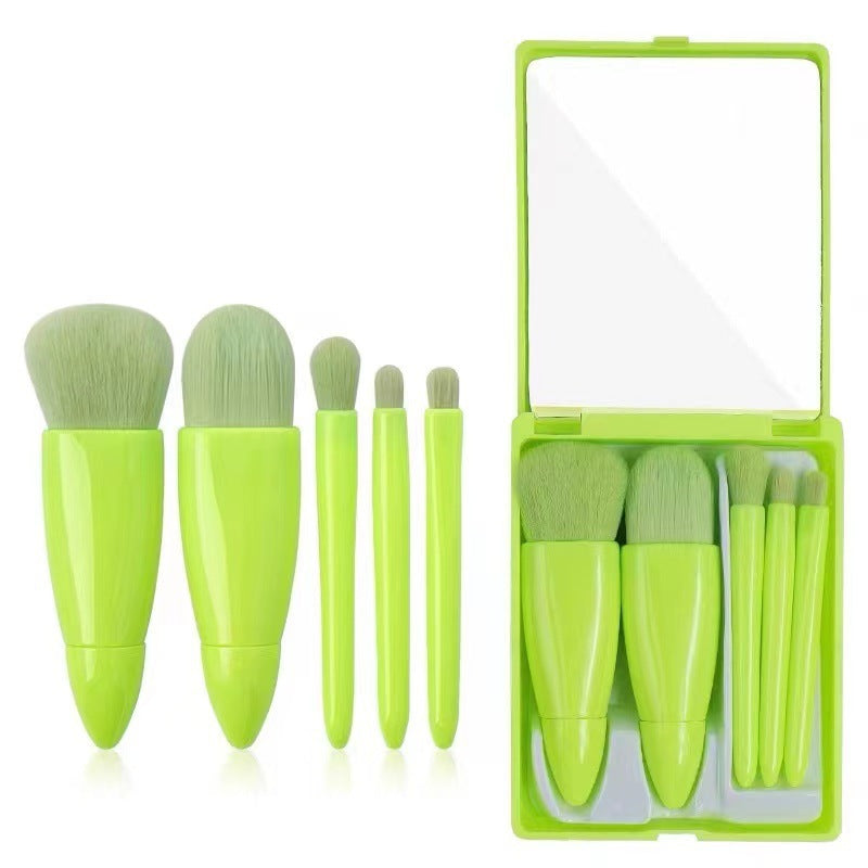 Set of green makeup brushes with a clear mirror case on a white background