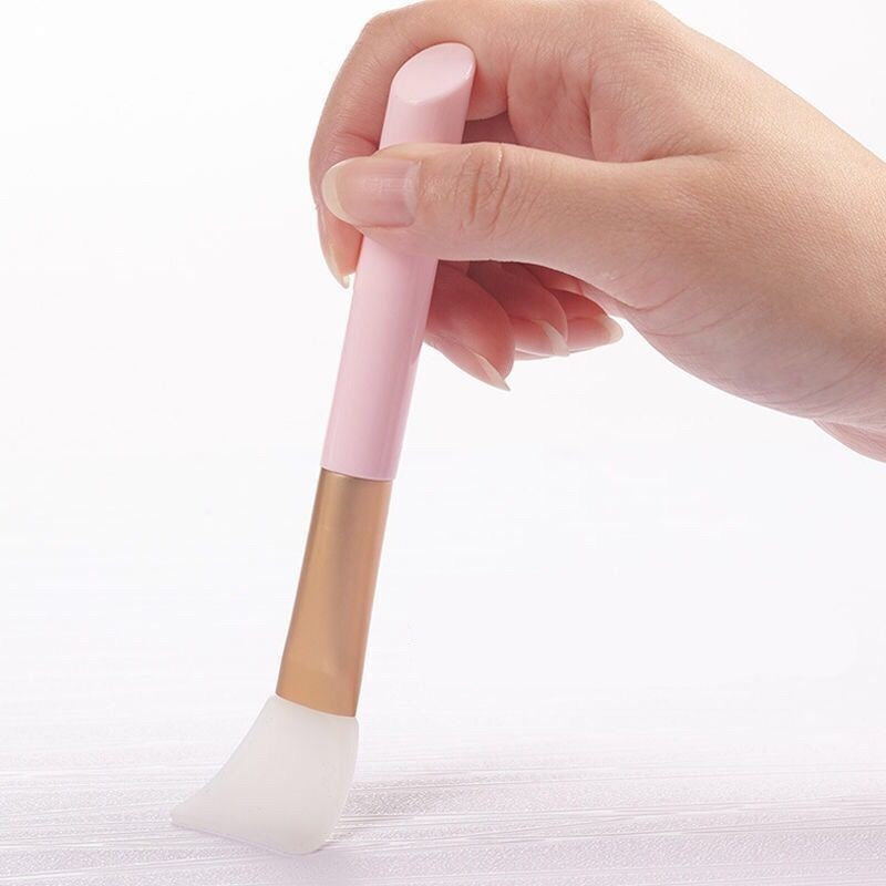 Hand holding a pink and gold makeup brush on a white background